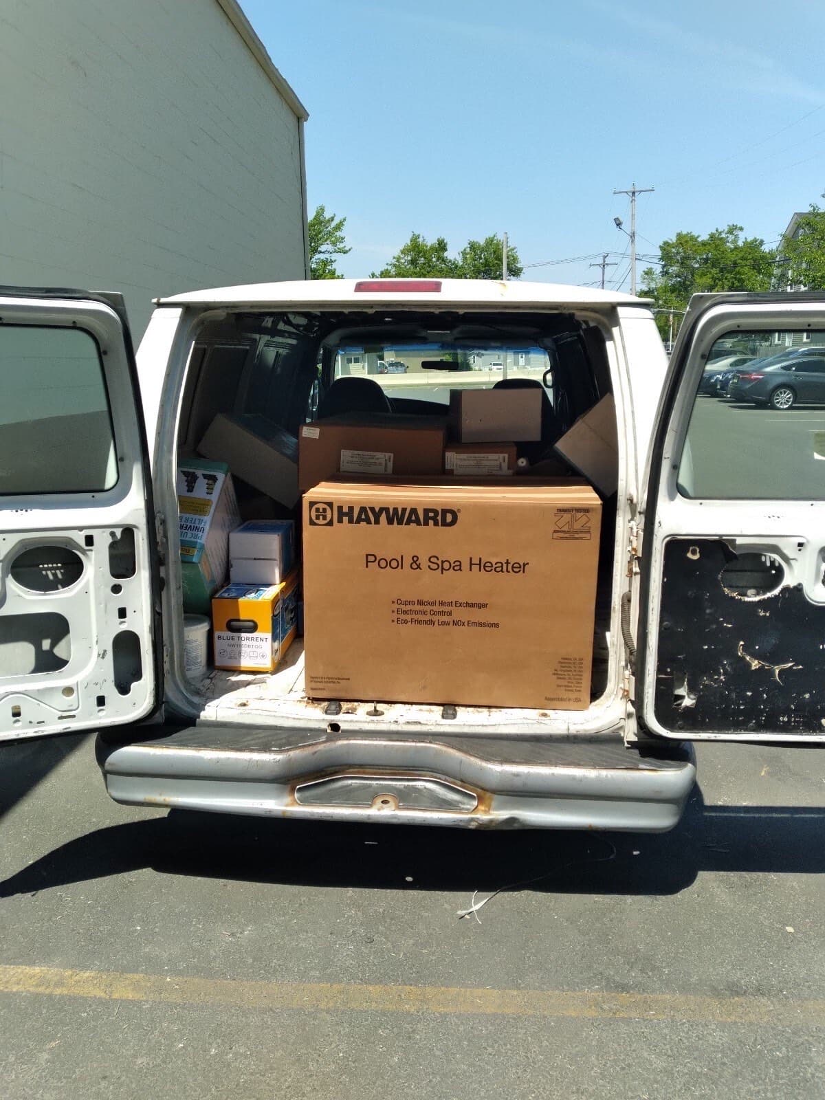 Rear of a white cargo van with doors open and a Hayward pool heater box loaded inside, ready for a Curri same-day Sprinter or cargo van delivery