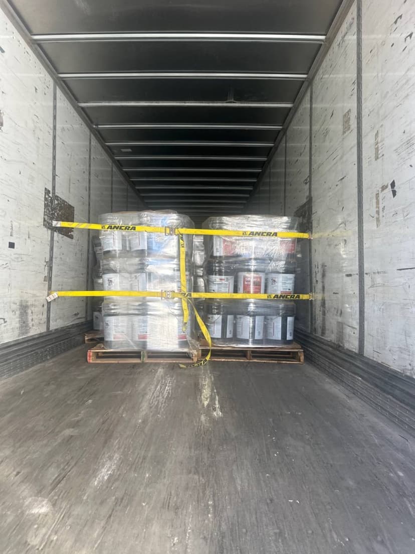 Pallets of paint cans strapped down inside a dry van trailer for a Curri building-materials run