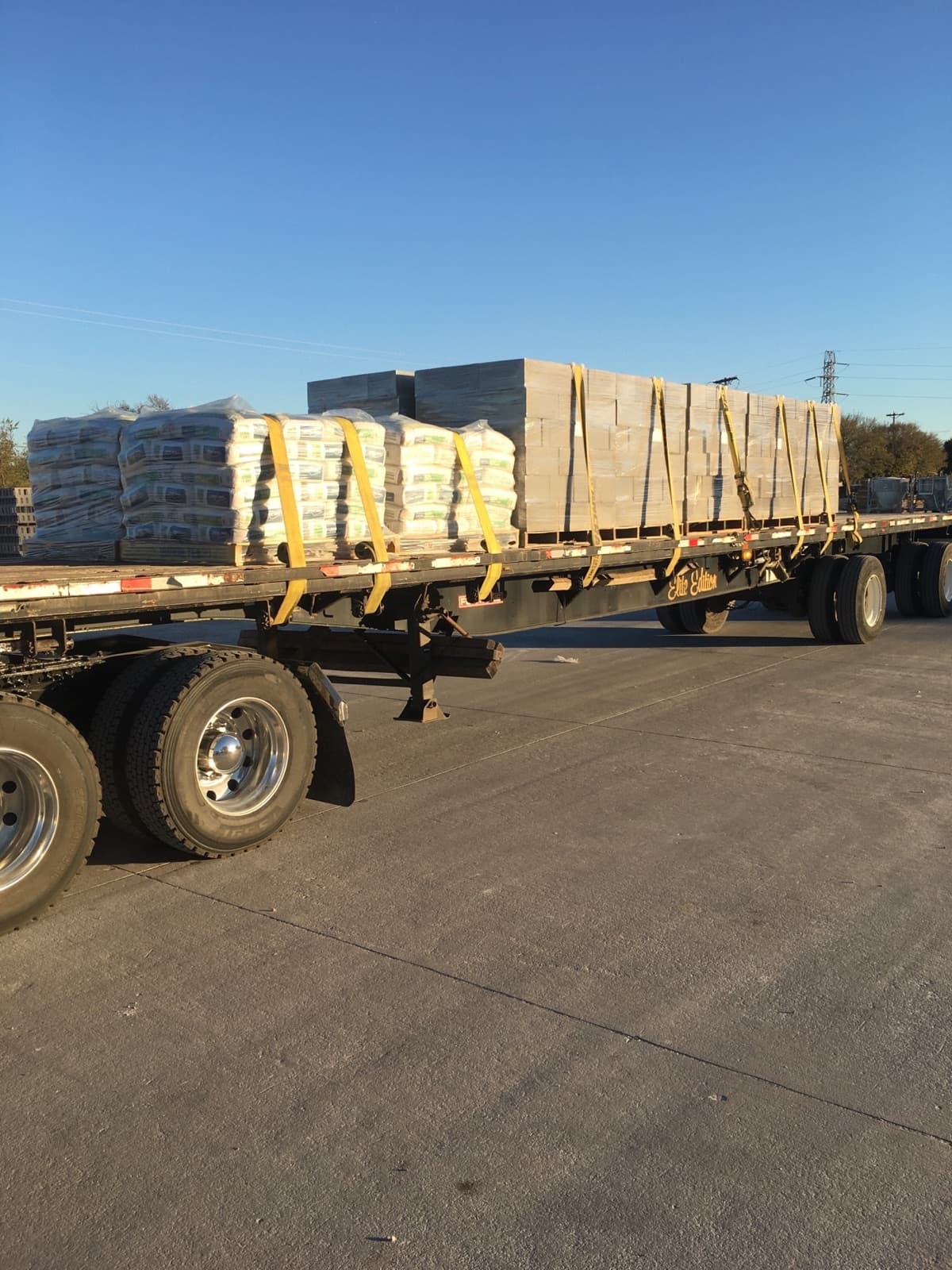 Flatbed loaded with cement bags and lumber bundles strapped down for a Curri heavy-materials haul