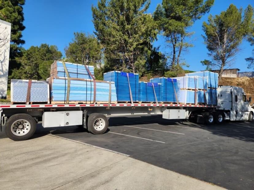 Flatbed semi loaded with stacked blue insulation panels for a Curri same-day delivery to a customer site