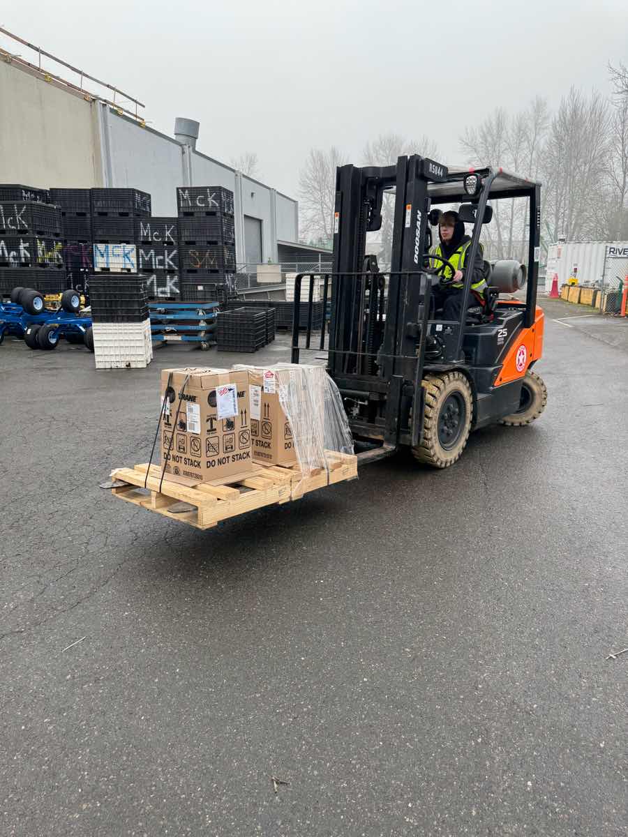Forklift operator in hi-vis lifting crated cargo at a Curri Moffett delivery site