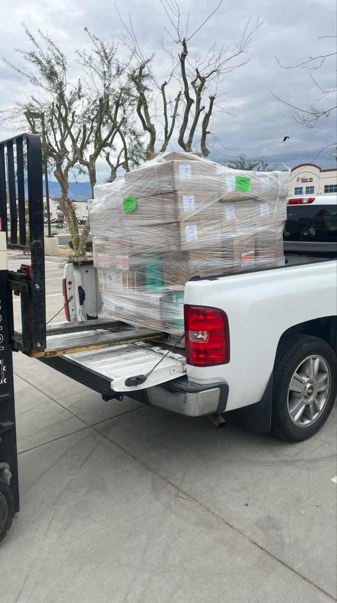 Forklift loading a shrink-wrapped pallet into the bed of a white pickup truck for a Curri same-day supply pickup