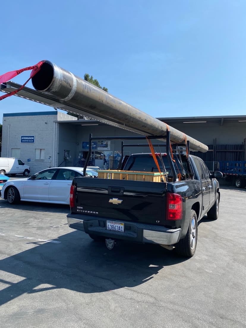 Black Chevy Silverado pickup with overhead pipe rack hauling long black pipe for a Curri same-day delivery