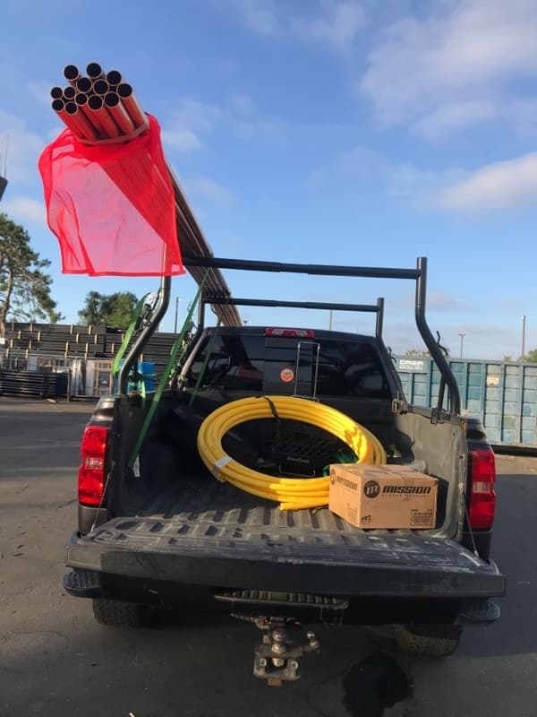 Pickup bed loaded with red PVC pipes in a safety bag and yellow electrical conduit for a Curri same-day supply run
