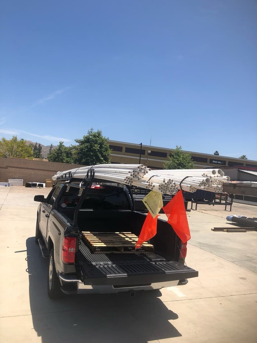 Dark pickup with a bundle of white PVC plumbing pipe strapped to its overhead pipe rack for a Curri same-day delivery