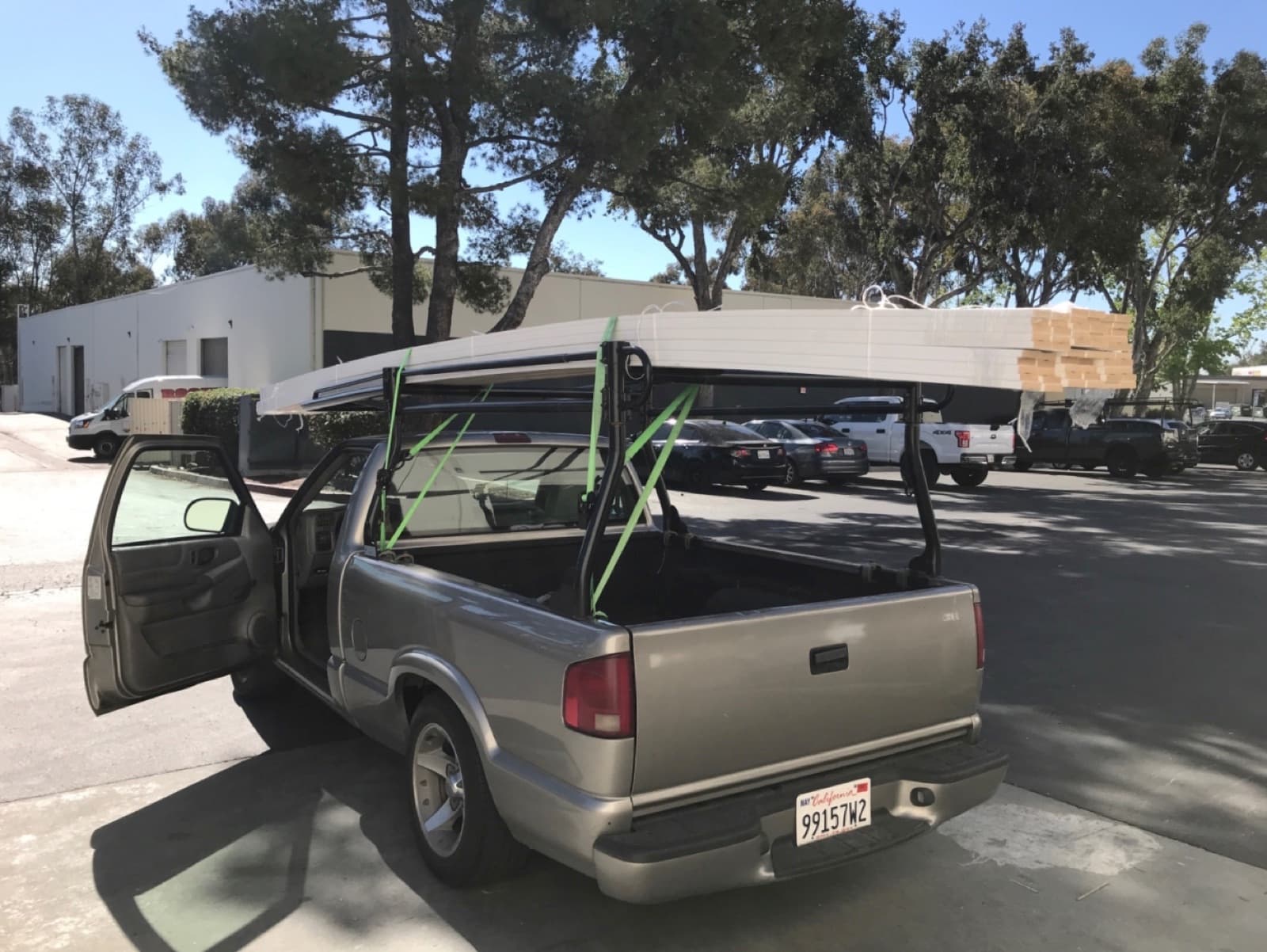 Tan Chevy S-10 pickup carrying flat aluminum panels on its pipe rack for a Curri same-day materials delivery