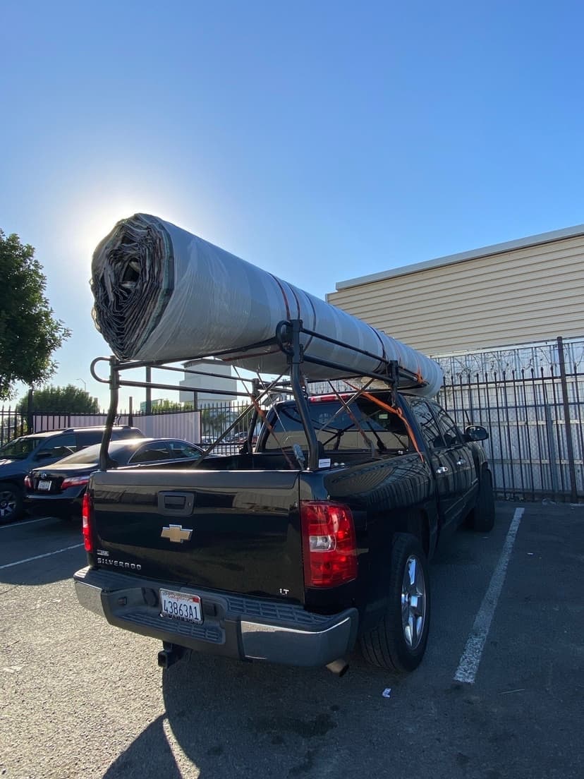 Black Silverado pickup with a wrapped roll of insulation strapped to the pipe rack for a Curri same-day drop-off