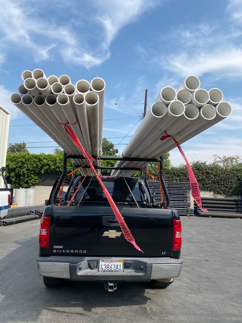 Black Silverado loaded with white PVC pipe bundles on the overhead rack ready for a Curri plumbing-supply route