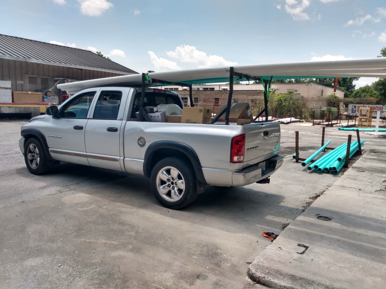 Silver Dodge Ram with teal-painted pipe loaded on the rack at a supply yard for a Curri pickup-truck delivery
