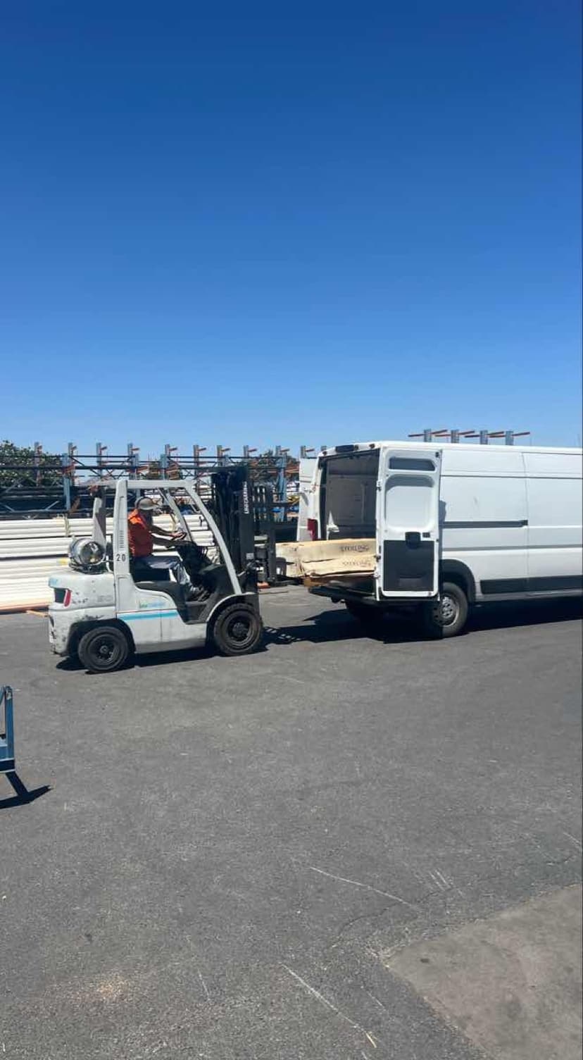 Forklift loading bundled lumber through the rear doors of a white Sprinter Van for a Curri same-day pickup