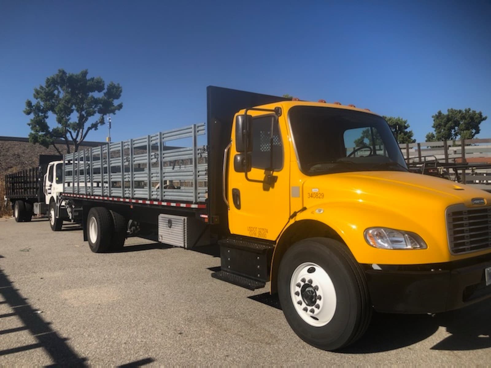 Yellow Curri Freightliner stakebed truck with tall galvanized stake rails along the bed, parked in a sunny lot ready for a same-day open-bed delivery