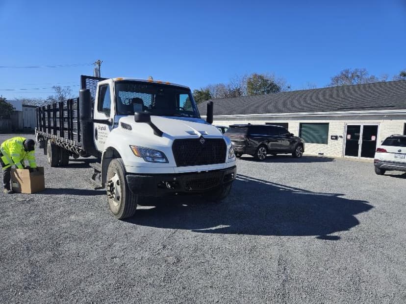 White stakebed truck staged in a parking lot under blue sky with a driver in a safety vest ready for a Curri same-day delivery