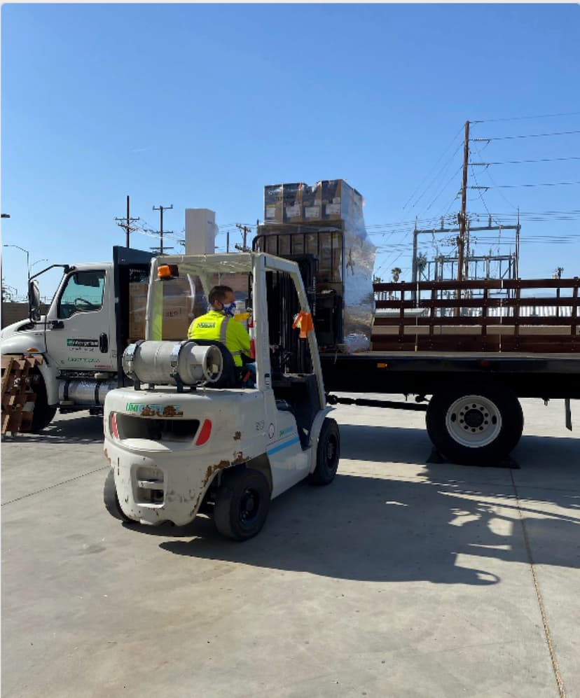 Forklift loading boxed materials onto a wood-rail stakebed truck for a Curri same-day pickup