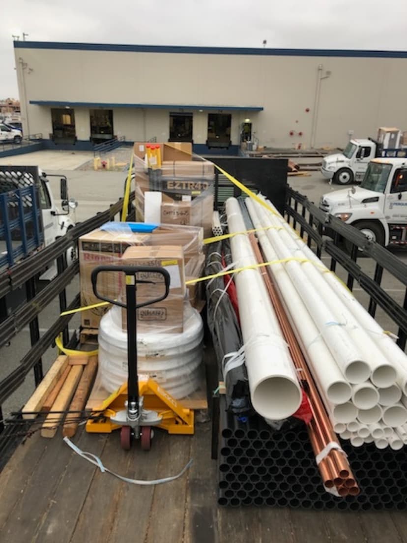 Stakebed loaded with bundles of PVC and copper pipe alongside a pallet jack for a Curri same-day supply delivery